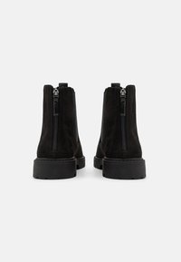 Botines de ante negro con un acabado suave, que cuentan con cremalleras laterales y suelas de goma negra resistentes para ofrecer tracción y durabilidad.