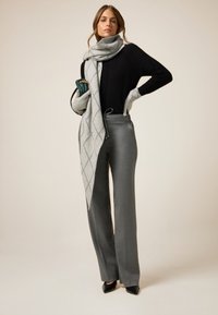 Pantalones de mezcla de lana gris con una bufanda de patrón gris claro a juego. La parte superior es un suéter negro con detalles texturizados. Los tacones negros completan el conjunto.