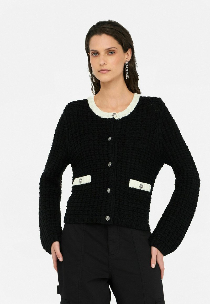 Schwarze Strickjacke mit einem weißen Kragen, großen Knöpfen und Fronttaschen. Strukturiertes Material mit einer kastigen Passform und langen Ärmeln.