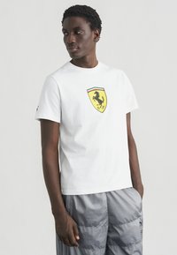Λευκό βαμβακερό t-shirt με στρογγυλή λαιμόκοψη που διαθέτει πολύχρωμο λογότυπο Ferrari στο στήθος. Κοντά μανίκια, άνετη γραμμή.
