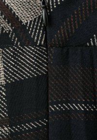 Primer plano de tela negra con un patrón geométrico en tonos blanco y marrón, con un detalle de cremallera en un lado.