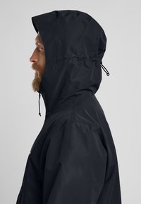 Sorte vandtætte jakke med høj krave, justerbar hætte og snoretræk. Har en glat tekstur og minimalistisk design.