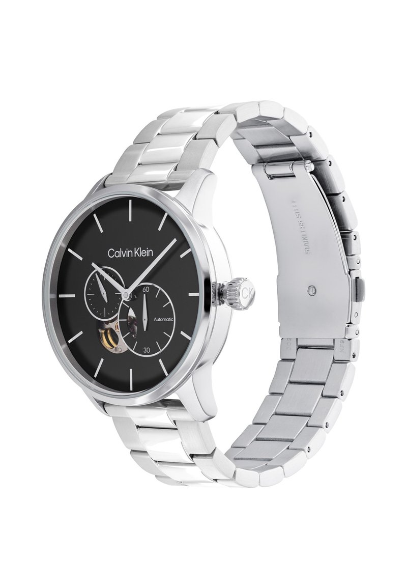 Reloj de acero inoxidable plateado con esfera redonda negra, que presenta dos subesferas y una corona. La correa está compuesta por segmentos de metal enlazados.
