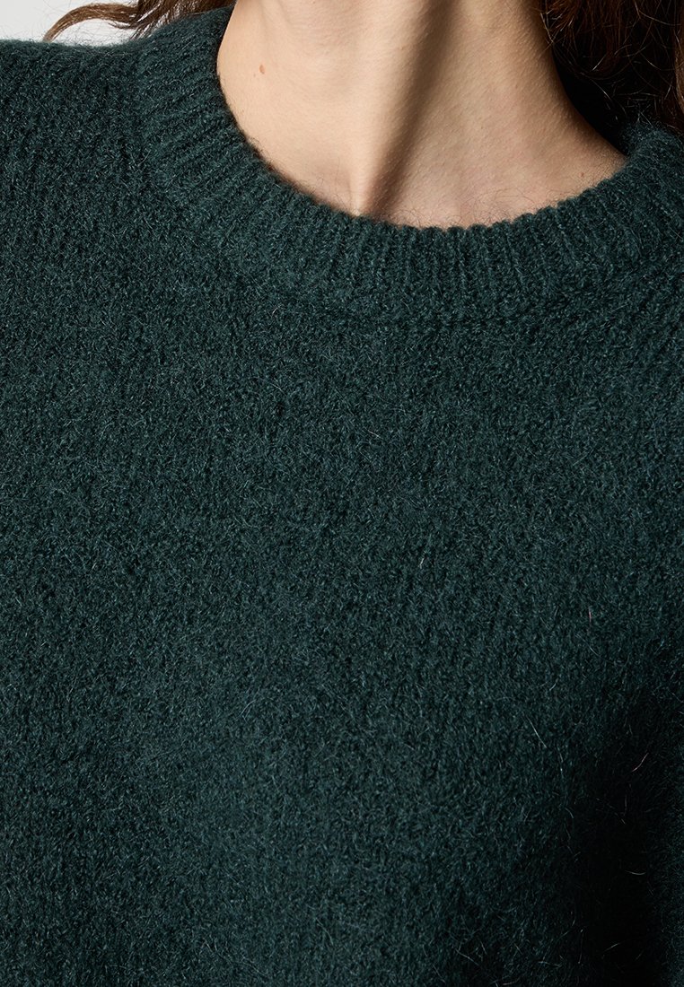 Dunkelgrüner gestrickter Pullover mit einem gerippten Rundhalsausschnitt. Die Textur wirkt weich und flauschig, typisch für Wolle oder ein ähnliches Material.