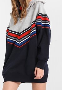 Sudadera con capucha en gris y azul marino, con rayas en forma de chevron en rojo, azul y blanco. Material de algodón con un corte relajado y puños de canalé.