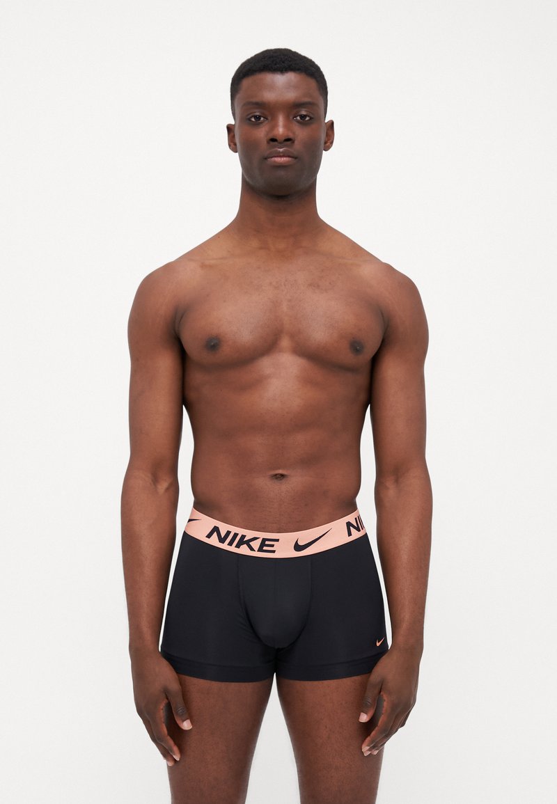 Black boxer briefs with a peach Nike logo waistband. The material appears smooth and fitted, highlighting a tailored design.