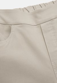 Beige tyg med en slät textur, med en elastisk midjeband och en sidoficka med synliga söm detaljer.