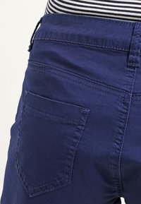 Tmavě modré bavlněné kraťasy s kapsou na zadní stran�ě, viditelným švem a pruhovaným pasem. Mají uvolněný střih a hladkou texturu.