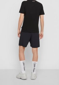 Svart bomulls t-shirt, mörkblå shorts, vita strumpor med "Calvin Klein" tryck. Modern design, slim fit, mjuk textur och monokrom färgschema.