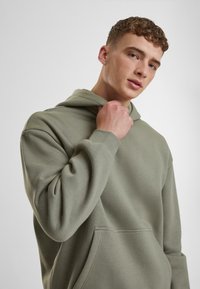 Sudadera verde claro hecha de una tela suave, con un bolsillo frontal y capucha ajustable, de corte relajado y detalles de diseño minimalistas.
