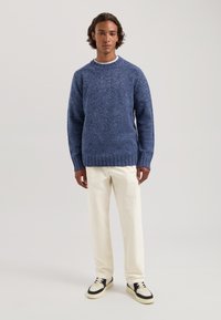 Marineblauw gebreid trui met een gestructureerde afwerking, ronde halslijn, geribde mouwen, gecombineerd met crèmekleurige broeken en sneakers met marineblauwe accenten.