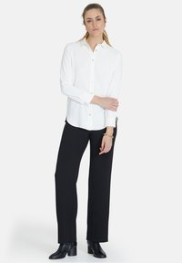 Cămașă albă cu guler, mâneci lungi și slituri laterale, purtată cu pantaloni negri cu picioare largi și cizme cu toc negre până la gleznă.
