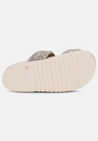 Voetbed van een sandaal met beige textuurmateriaal met een gevlekt patroon en een witte rubberen zool met groeven voor extra grip.