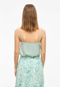 Camiseta de satén verde menta con tirantes ajustables, combinada con una falda estampada que presenta diseños de pajaritas en verde y aqua.