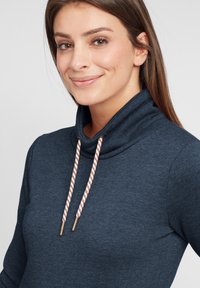Mörkblå topp med cowl-neck i mjukt material, med randiga dragsko med metallspetsar och en figurnära silhuett.