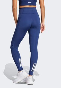 Marineblaue hochtaillierte Leggings mit weißen Drei-Streifen-Akzenten. Hergestellt aus dehnbarem Material, mit einem figurbetonten Design und subtilen Nahtdetails.
