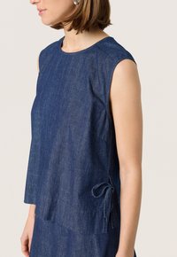 Blue denim sleeveless top with a round neckline, loose fit, and side tie detail. Smooth texture, lightweight fabric, and casual design.