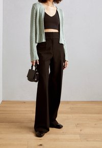 Mintgrön stickad cardigan, svart crop top, svarta vida byxor, håller en liten svart handväska, släta texturer och avslappnad passform.