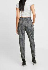 Kostičkované kalhoty v černobílé barvě, s vysokým pasem, předními kapsami a pohodlným střihem, doplněné černými na vysokém podpatku.