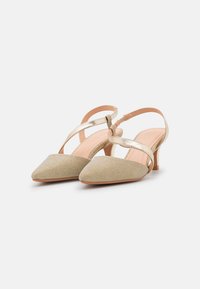 Chaussures à talons slingbacks beiges à bout pointu, avec une tige en tissu texturé et des brides métalliques, dotées d'un talon bas et fin.
