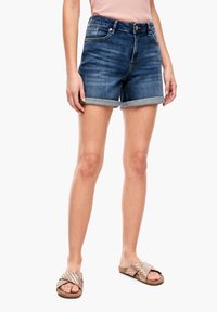 Shorts en denim, délavage bleu moyen, ourlet retroussé, design à cinq poches, associés à des sandales à glisser tissées en ton or rose. Texture lisse.