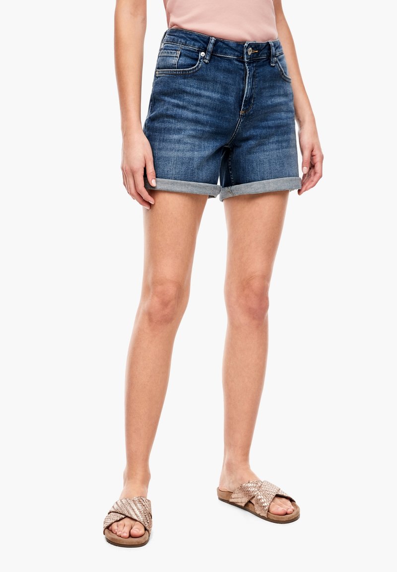 Shorts en denim, délavage bleu moyen, ourlet retroussé, design à cinq poches, associés à des sandales à glisser tissées en ton or rose. Texture lisse.