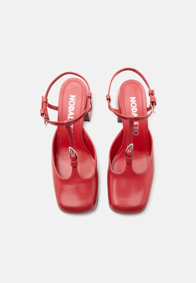 Κόκκινες δερμάτινες γόβες slingback με τετράγωνα μύτη και ρυθμιζόμενα λουράκια στον αστράγαλο, φωτογραφημένες από πάνω σε λευκό φόντο.