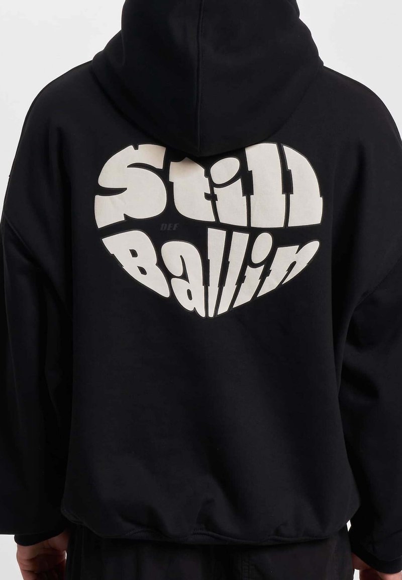 Czarna bluza z kapturem z dużą białą grafiką na plecach z napisem "Still Ballin." Miękka tkanina i luźny krój.