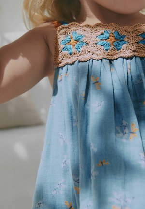 Blå ärmlös klänning med en brun och blå crochéerad bodice, prydd med blommönster i orange och lila på ett lätt tyg.