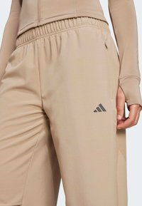 Beżowe spodnie sportowe z elastycznym pasem, szarym logo i bocznymi kieszeniami. Wykonane z miękkiego, gładkiego materiału o luźnym kroju.
