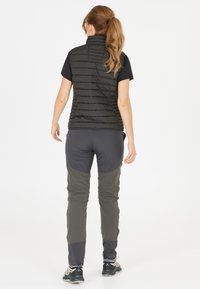 Schwarzige gepolsterte Weste mit hohem Kragen, kombiniert mit grauen und olivgrünen Hosen, die kontrastierende Paneeldetails aufweisen. Eignet sich für Outdoor-Aktivitäten.