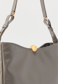 Szürke bőr kézitáska sima felülettel, arany kör alakú kapoccsal és arany díszítésű állítható pánttal. Egyszerű, modern kialakítás.