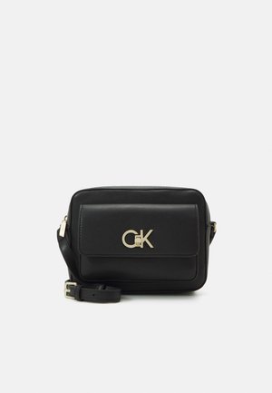 Bolso rectangular negro de bandolera con logo CK dorado en el bolsillo frontal y correa ajustable con hebilla dorada.