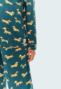 Pijama de manga larga en tela de color azul oscuro con un patrón repetitivo de dachshund. Presenta una etiqueta en el lateral y detalles de ribete en contraste.