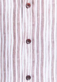 Tissu rayé verticalement beige et blanc avec trois boutons à quatre trous brun foncé cousus le long de la couture centrale.