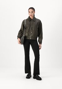 Roheline, läikiv bomber jacket krae, lukuga küljetaskud ja elastsed varrukad, koos mustade laienevate pükste ja mustade kingadega.