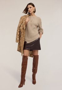 Beige kabelstickad tröja, brun imitation läder mini kjol, mönstrad sandfärgad kappa, och bruna knähöga klackstövlar med spetsiga tår.