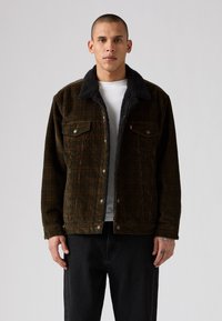Brown corduroy jacket with a black sherpa collar. Features two front pockets, front buttons, and a relaxed fit. Worn over a white shirt.