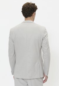 Light gray tailored suit jacket with a smooth fabric, notched lapels, and double back vents. Features two side pockets and buttoned cuffs.