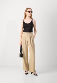 Black sleeveless top with shiny texture and decorative straps, paired with beige tailored wide-leg trousers and black pointed-toe heels.