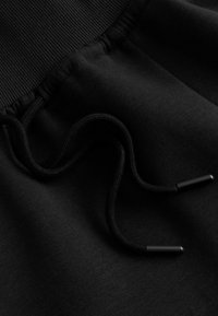 Gros plan sur un tissu noir avec une ceinture côtelée et un cordon noir avec embouts en plastique sur un vêtement.