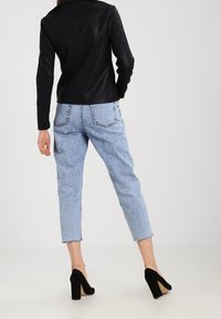 Chaqueta de cuero negra sobre jeans de cintura alta de color azul claro con dobladillos deshilachados, combinada con zapatos de tacón negro. Vista trasera visible.