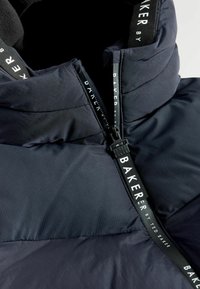 Chaqueta aislante azul marino con cuello alto, cierre de cremallera con tirador de marca y una textura suave con detalles acolchados.