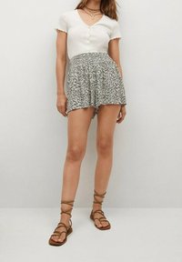 Top blanco de manga corta con textura acanalada y detalles de botones, combinado con una falda fluida de estampado floral. La modelo lleva sandalias marrones con cordones.