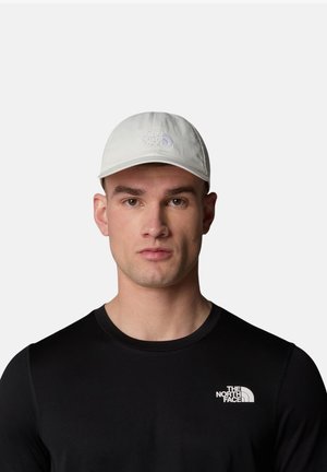 Light gray cotton cap with a curved brim, featuring an embroidered logo on the front. Model wearing a black shirt with a visible logo.