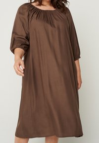Robe marron jusqu'aux genoux, en tissu lisse, avec un col arrondi, une taille froncée et des manches bouffantes avec des poignets élastiques.