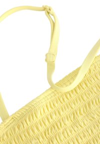 Keltainen smokkikangas ylin, jossa on säädettävät hihnat. Materiaali on pehmeää ja hieman teksturoitua, ja siinä on poimittu muotoilu pinnalla.