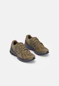 Chaussures de sport vert olive avec un design en mesh, des accents texturés, et une semelle grise coussinée, munie d'un bout arrondi et d'un système de laçage.