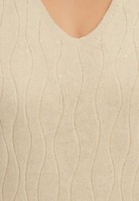 Maglione beige lavorato a maglia con scollatura a V profonda, motivo a onde e delicati luccichii sparsi nel tessuto, creando un aspetto texturizzato.