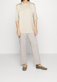 Beige satin top med korte ærmer og rund halsudskæring, parret med lysegrå, løs pasform bukser og grønne flade sko. Simpel design.